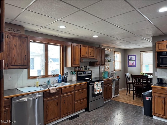 kitchen featuring tile countertops, tasteful backsplash, appliances with stainless steel finishes, a sink, and under cabinet range hood