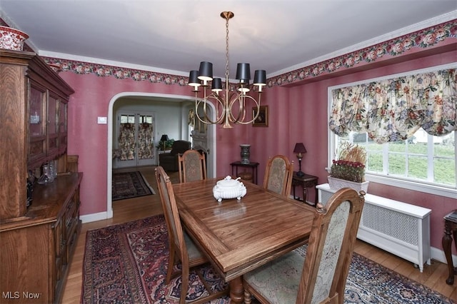 dining room with baseboards, arched walkways, radiator, wood finished floors, and a notable chandelier