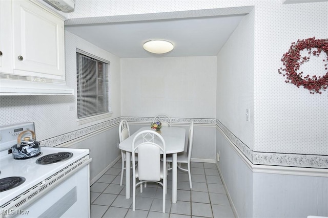 kitchen with a wainscoted wall, electric range, light tile patterned floors, and under cabinet range hood