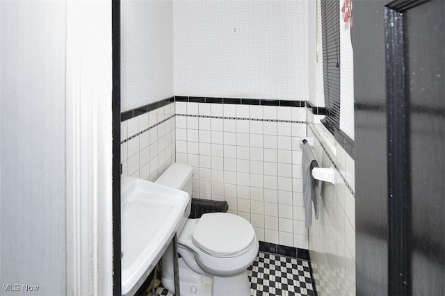 half bathroom featuring toilet, a sink, tile walls, wainscoting, and wallpapered walls