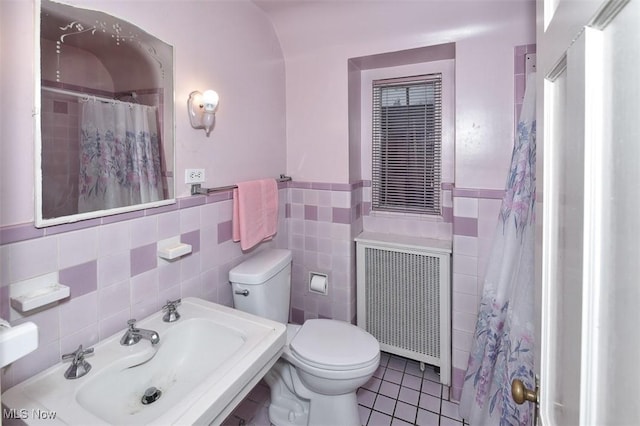 bathroom featuring tile patterned flooring, toilet, a sink, tile walls, and radiator