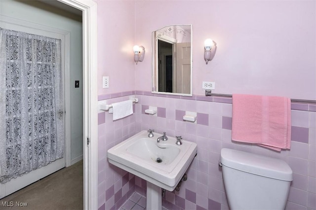 bathroom with toilet, tile walls, and wainscoting