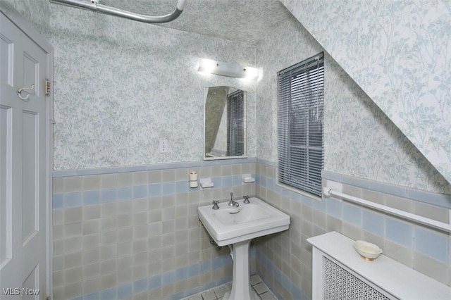 bathroom featuring wallpapered walls, tile walls, and wainscoting