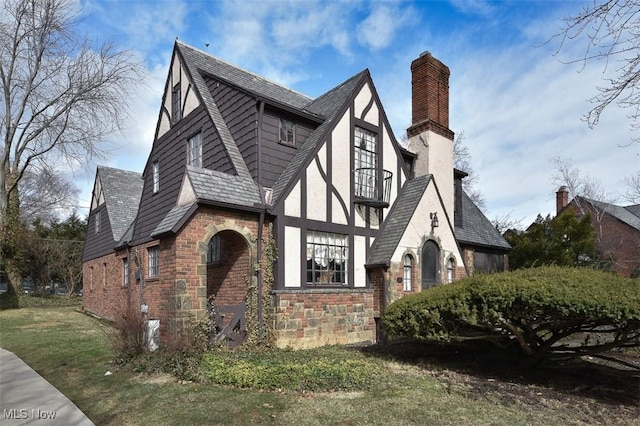 exterior space with a chimney, stucco siding, a balcony, stone siding, and a front lawn