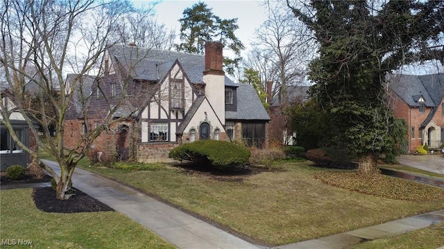 tudor home featuring stucco siding, a chimney, stone siding, and a front yard