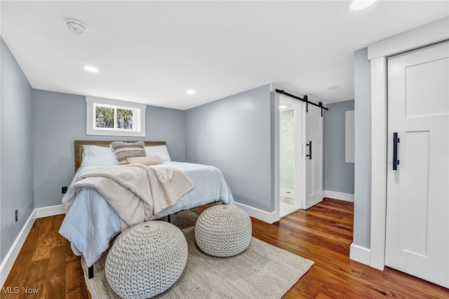 bedroom with a barn door, recessed lighting, wood finished floors, and baseboards