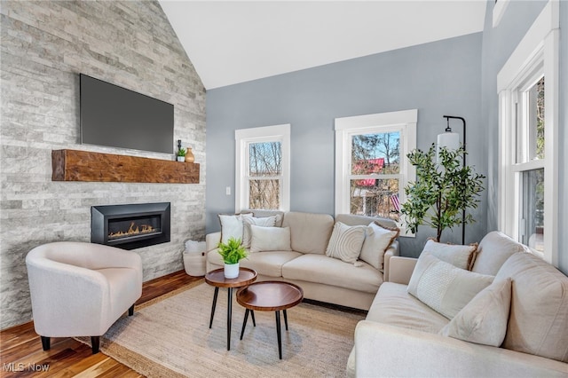 living room with high vaulted ceiling, wood finished floors, and a stone fireplace