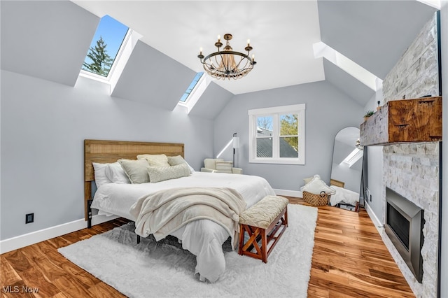 bedroom with lofted ceiling with skylight, a fireplace, wood finished floors, and baseboards