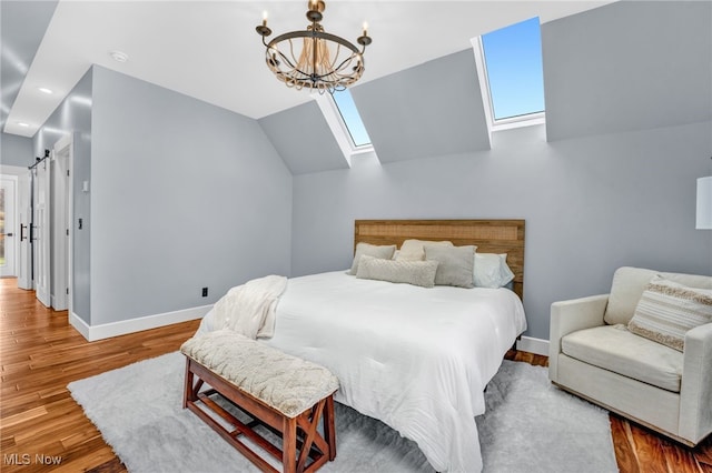 bedroom with vaulted ceiling with skylight, a barn door, baseboards, wood finished floors, and an inviting chandelier