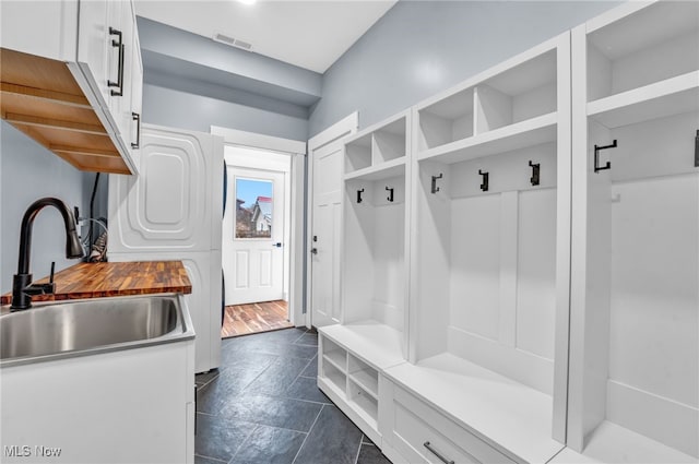 mudroom with stacked washer and dryer, visible vents, and a sink