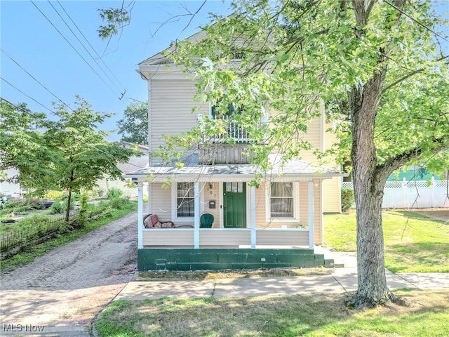 view of front facade featuring covered porch, a front yard, and fence