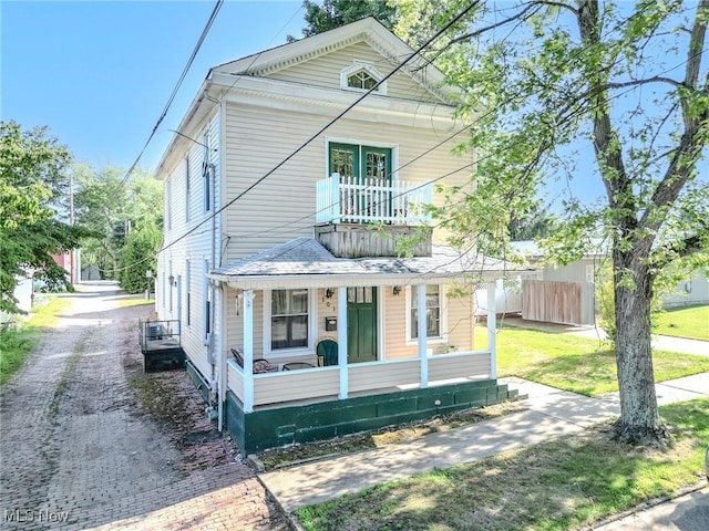 view of front of house featuring a front yard, covered porch, fence, and a balcony