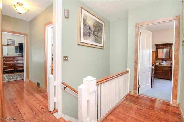 hall with wood finished floors and an upstairs landing