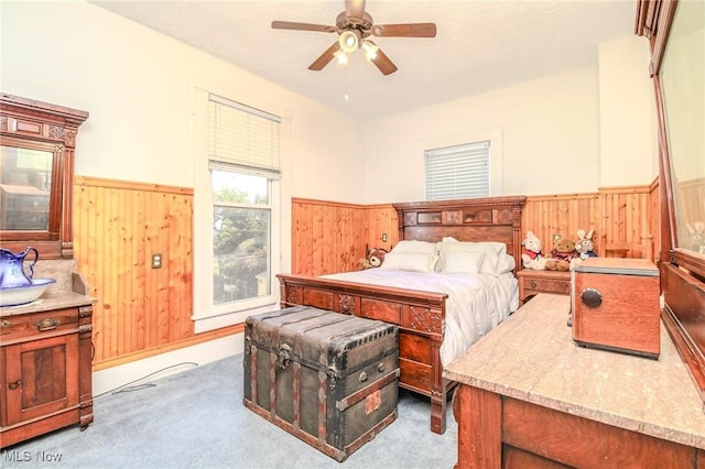 bedroom with a wainscoted wall, carpet, wooden walls, and a ceiling fan