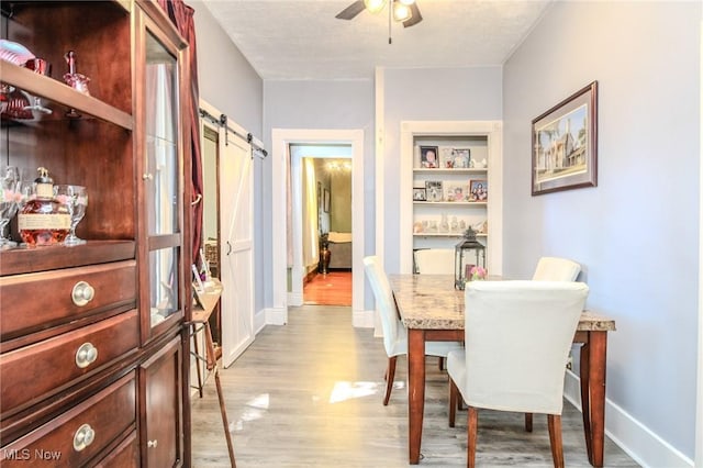 dining area featuring baseboards, a barn door, a ceiling fan, and light wood-style floors