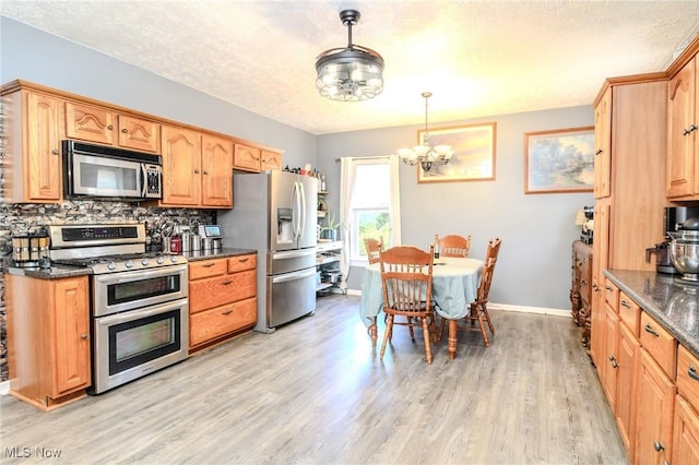 kitchen with light wood-style flooring, stainless steel appliances, baseboards, decorative backsplash, and dark stone countertops