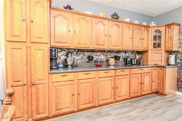 kitchen featuring a textured ceiling, light wood finished floors, glass insert cabinets, and tasteful backsplash