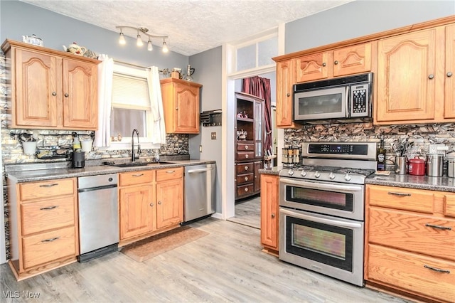 kitchen with stainless steel appliances, light brown cabinetry, a sink, a textured ceiling, and light wood-type flooring