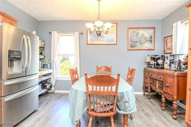 dining room with light wood-type flooring, a textured ceiling, baseboards, and a notable chandelier