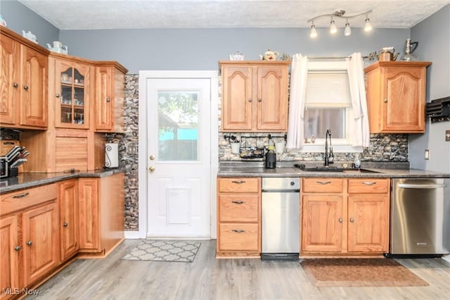 kitchen with light wood finished floors, dark countertops, backsplash, stainless steel dishwasher, and a sink