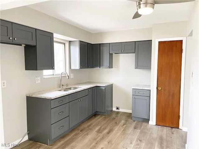 kitchen featuring light wood-type flooring, baseboards, gray cabinets, and a sink