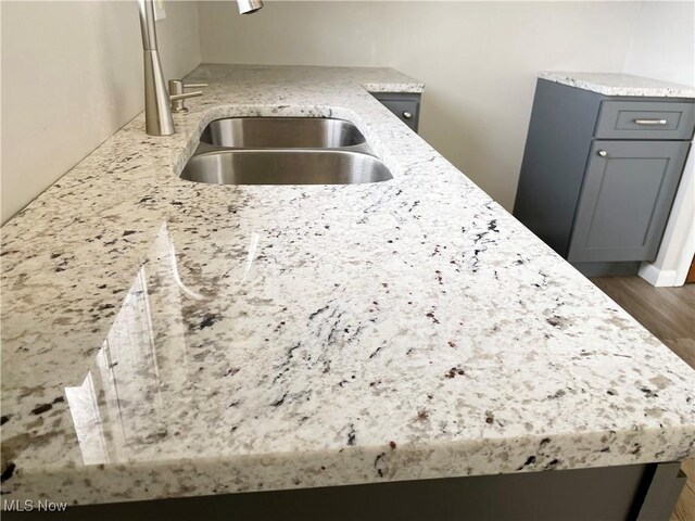 kitchen with light stone countertops, dark wood finished floors, a sink, and gray cabinetry