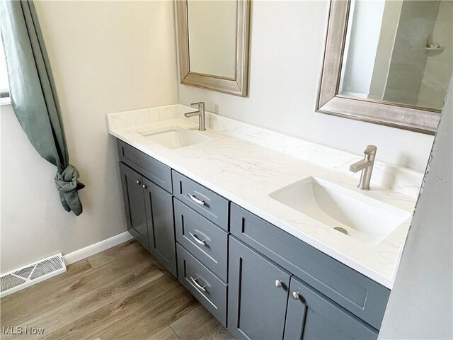 full bath with double vanity, wood finished floors, a sink, and visible vents