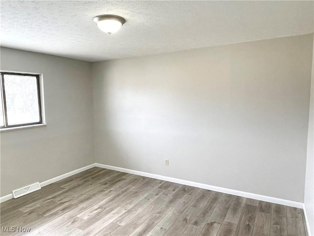 unfurnished room featuring baseboards, a textured ceiling, visible vents, and wood finished floors