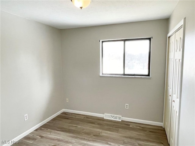 unfurnished bedroom with baseboards, a closet, visible vents, and wood finished floors