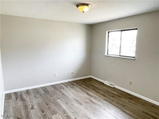 spare room featuring visible vents, baseboards, and wood finished floors