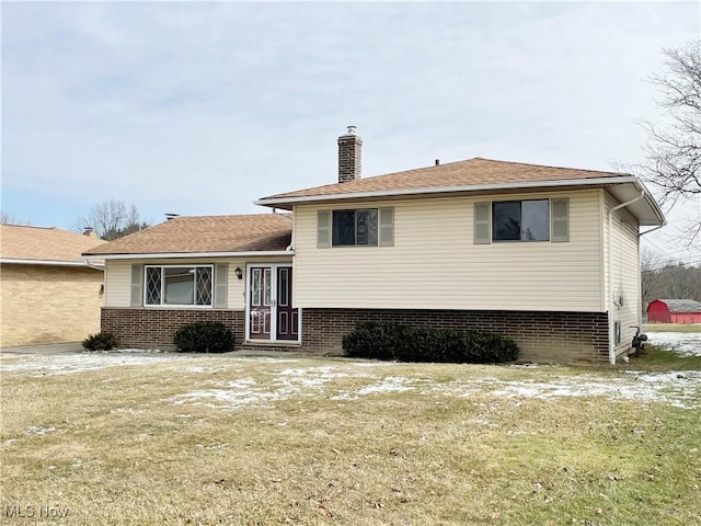 rear view of house with a yard, brick siding, and a chimney