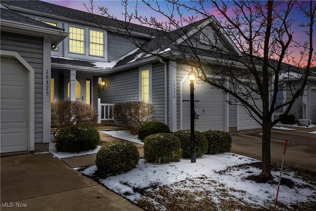 view of snowy exterior with an attached garage, driveway, and a shingled roof