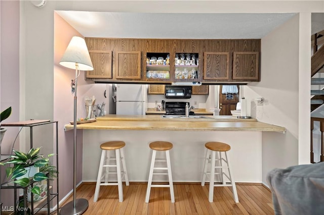 kitchen with freestanding refrigerator, light wood-type flooring, black microwave, range, and a peninsula