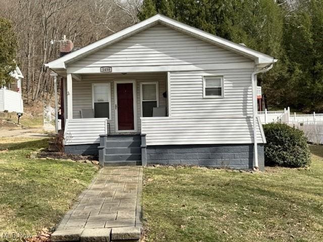 bungalow featuring covered porch, fence, and a front lawn