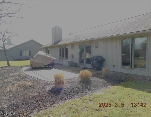 back of house with roof with shingles, a yard, a chimney, and a patio area