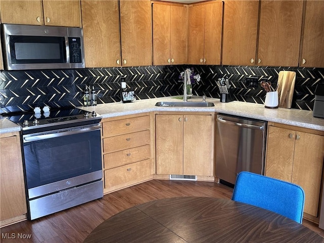 kitchen with tasteful backsplash, appliances with stainless steel finishes, dark wood-type flooring, and a sink