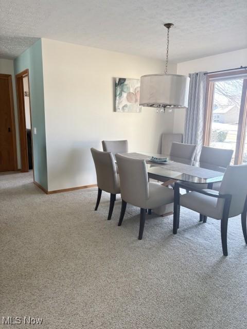 dining space with light carpet, baseboards, and a textured ceiling