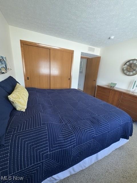 bedroom with carpet, a closet, visible vents, and a textured ceiling