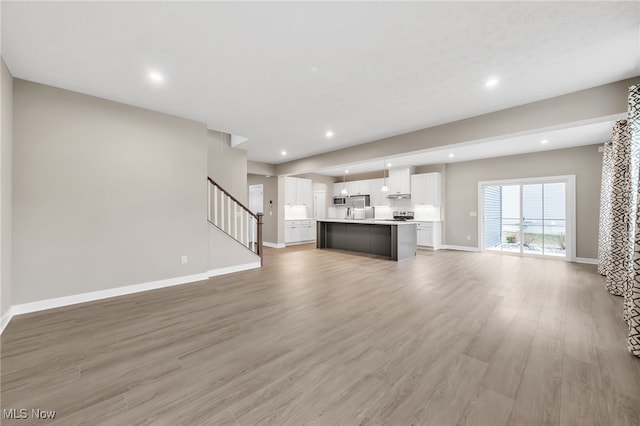 unfurnished living room with light wood-style floors, recessed lighting, baseboards, and stairs