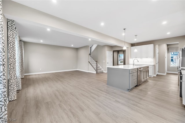 kitchen with gray cabinetry, a sink, light countertops, stainless steel dishwasher, and an island with sink