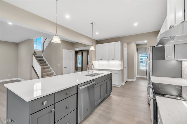 kitchen with a sink, appliances with stainless steel finishes, gray cabinets, decorative backsplash, and light wood finished floors