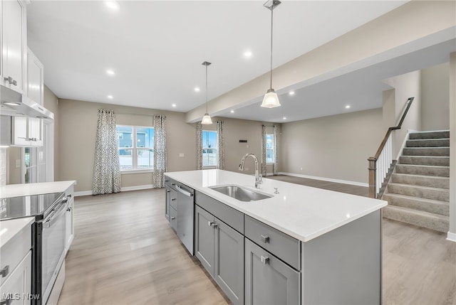 kitchen with appliances with stainless steel finishes, gray cabinets, light countertops, light wood-type flooring, and a sink