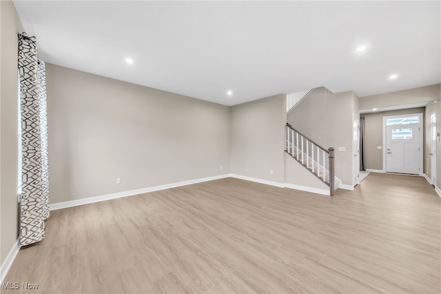 unfurnished living room featuring recessed lighting, baseboards, light wood finished floors, and stairs