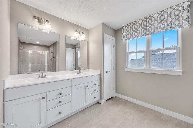 full bathroom with double vanity, a shower stall, baseboards, and a sink