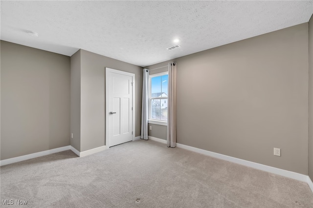 unfurnished room featuring light colored carpet, visible vents, baseboards, and a textured ceiling