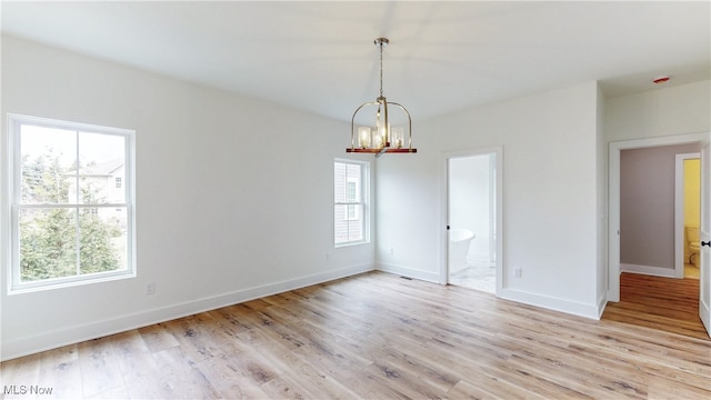 empty room with baseboards, light wood finished floors, and an inviting chandelier