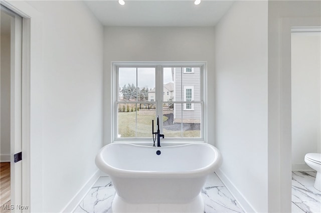 full bath featuring marble finish floor, a soaking tub, and baseboards