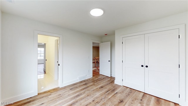 unfurnished bedroom featuring visible vents, a closet, light wood-style flooring, and baseboards