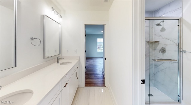 bathroom featuring baseboards, a sink, a marble finish shower, and double vanity