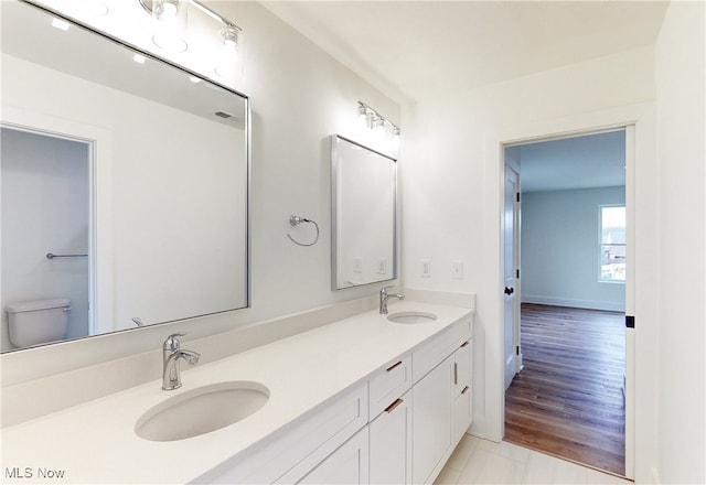 full bathroom with double vanity, a sink, toilet, and baseboards